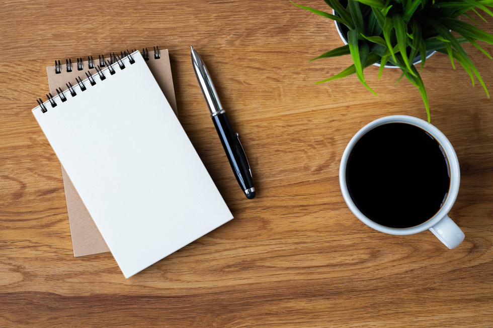 Top view of open school notebook with blank pages, coffee cup and pen for taking write notes on table background. Flat lay, creative workspace office. Business-education concept with copy space.